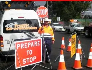 A Traffic Co-ordination van at a roadside job, with a controller holding a STOP bat beside a PREPARE TO STOP sign